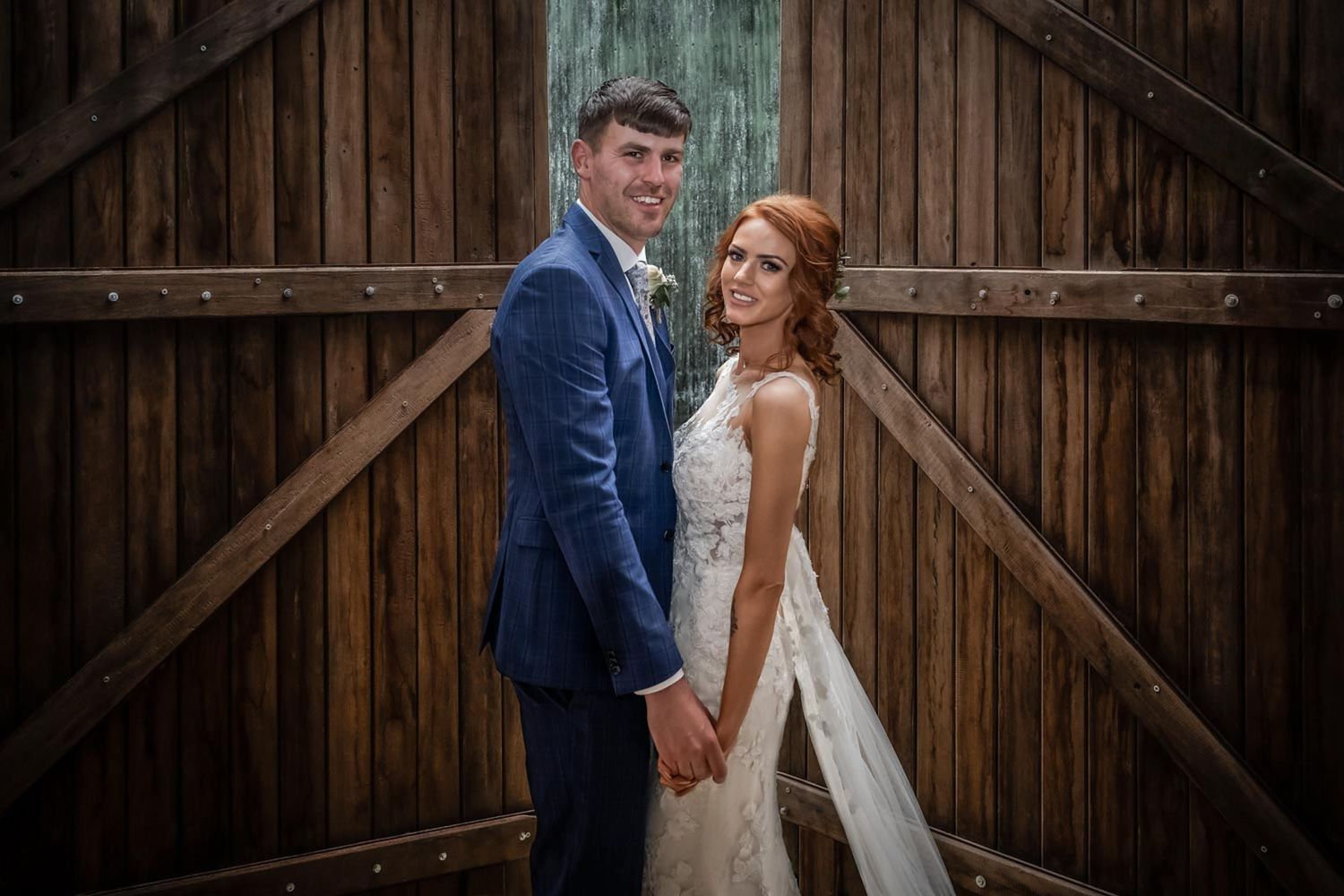 Couple in wedding attire posing against rustic wooden barn doors.