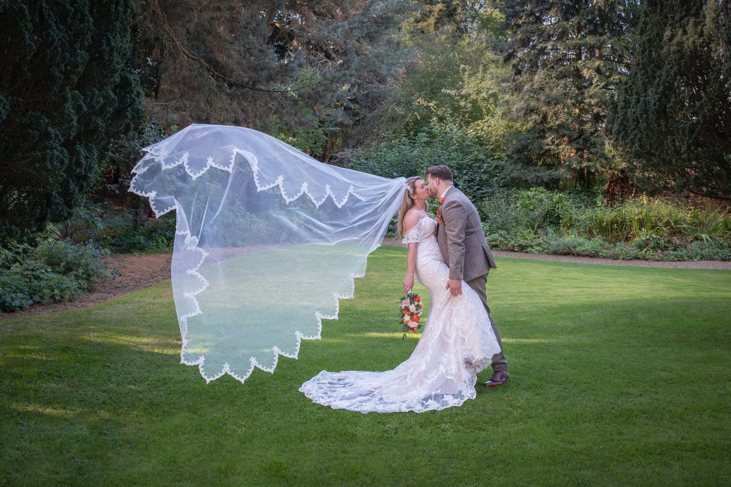 A dramatic wedding photo series with a flowing white lace dress spread across a manicured lawn.