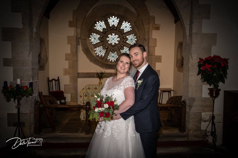 A wedding portrait inside a church sanctuary with a beautiful stained glass rose window in the background.