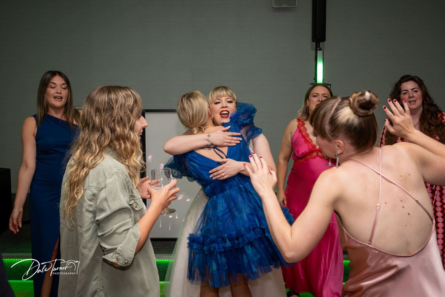 Dance floor scene at a wedding reception with guests in blue and pink formal attire.