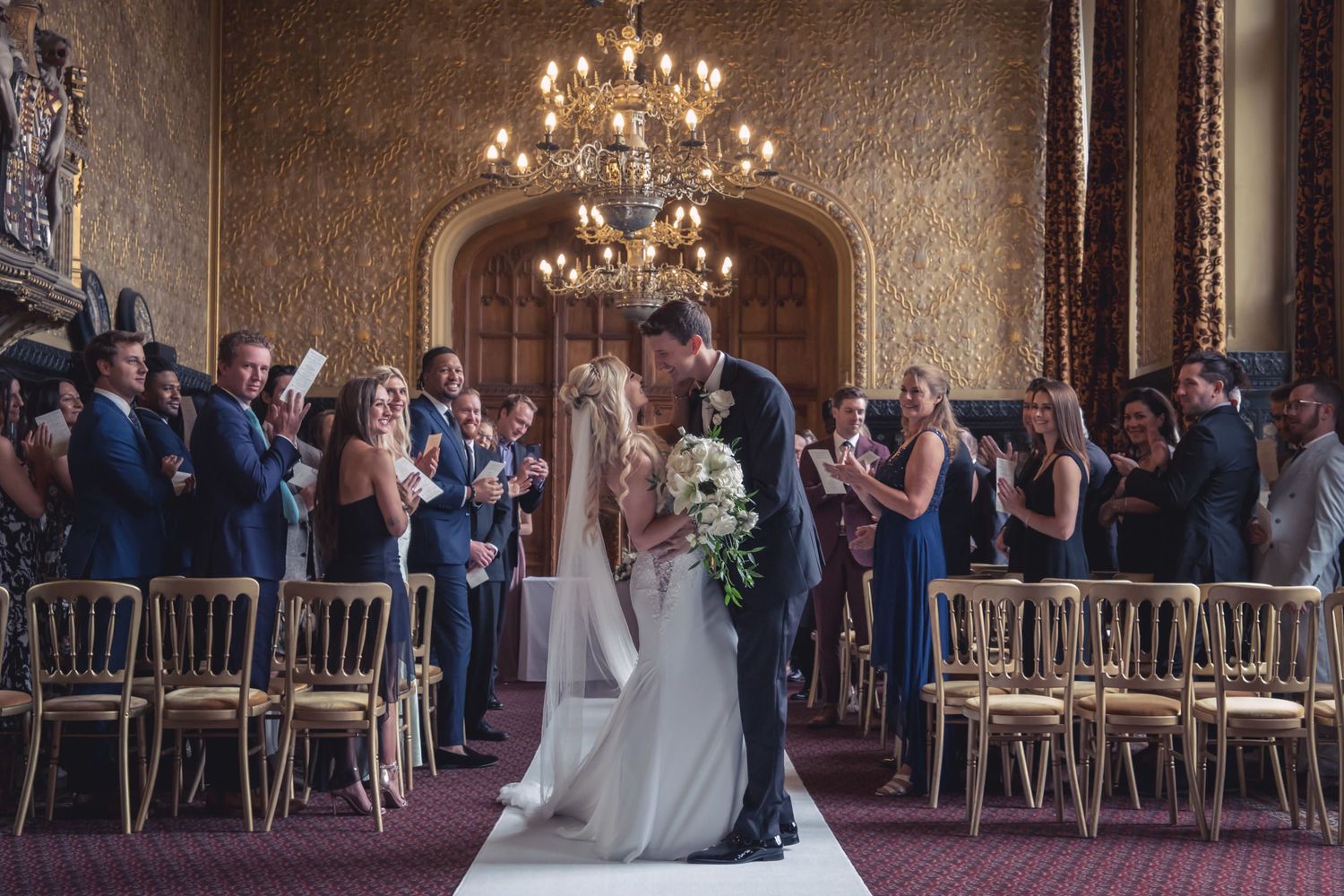 A wedding ceremony moment in an elegant hall with chandelier and gold chairs.