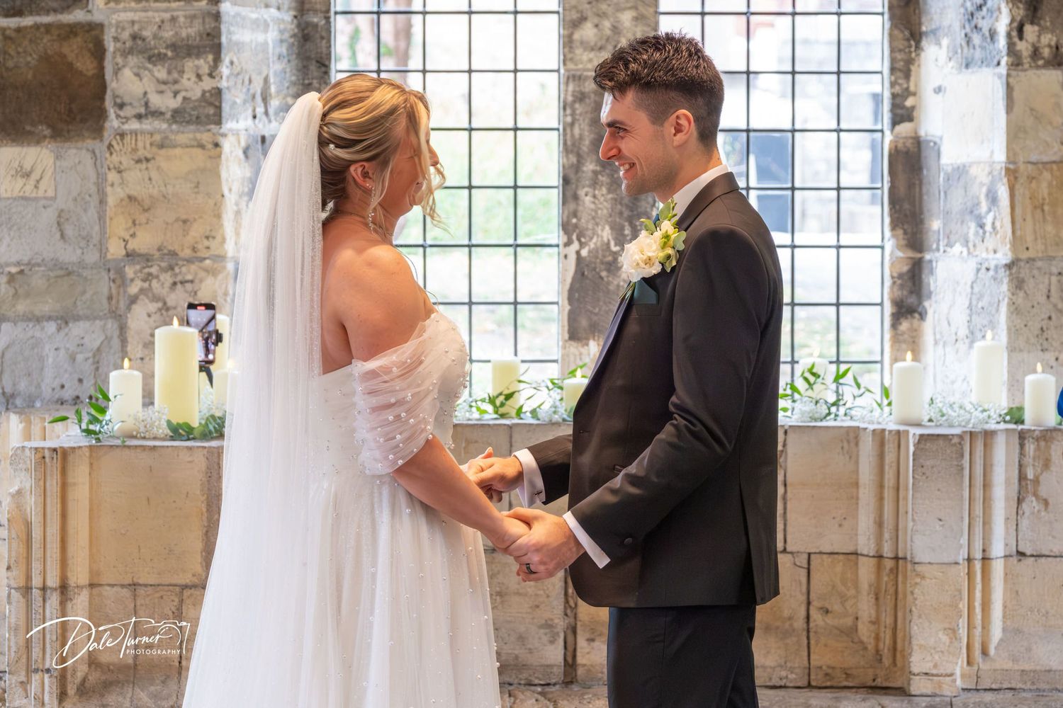Wedding ceremony exchange of rings in front of large church windows.