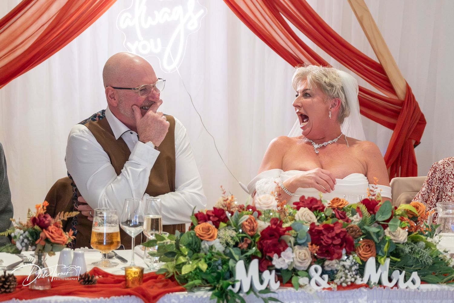 Wedding reception table decorated with red floral centerpieces and Mr. & Mrs. sign at head table.