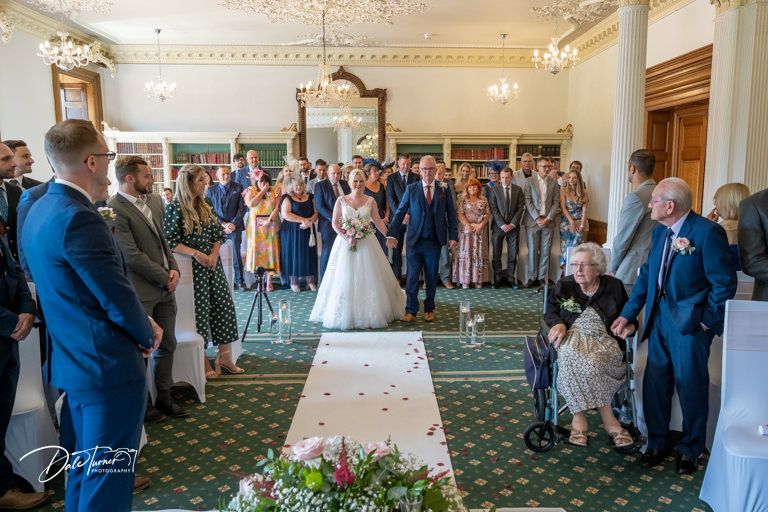 Wedding ceremony captured in panoramic view showing elegant room filled with guests.