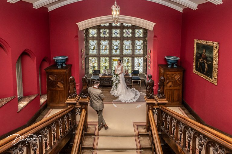 A romantic wedding scene on an elegant red-walled staircase with ornate details and vintage furnishings.
