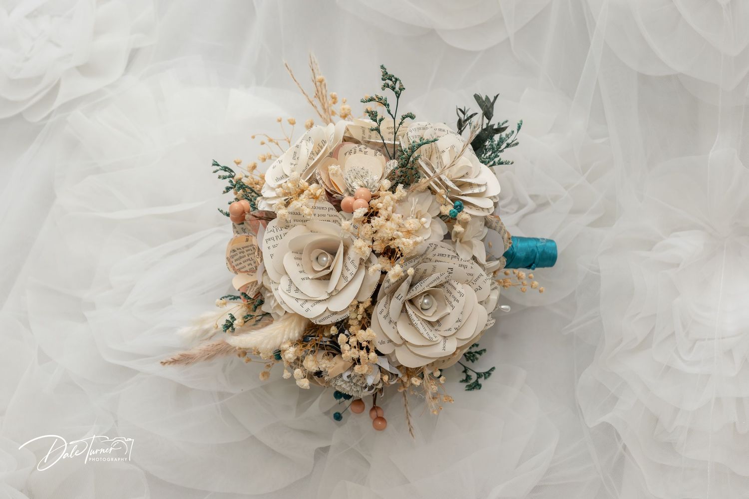 Elegant wedding bouquet with cream roses, dried flowers, and teal ribbon on white tulle fabric.