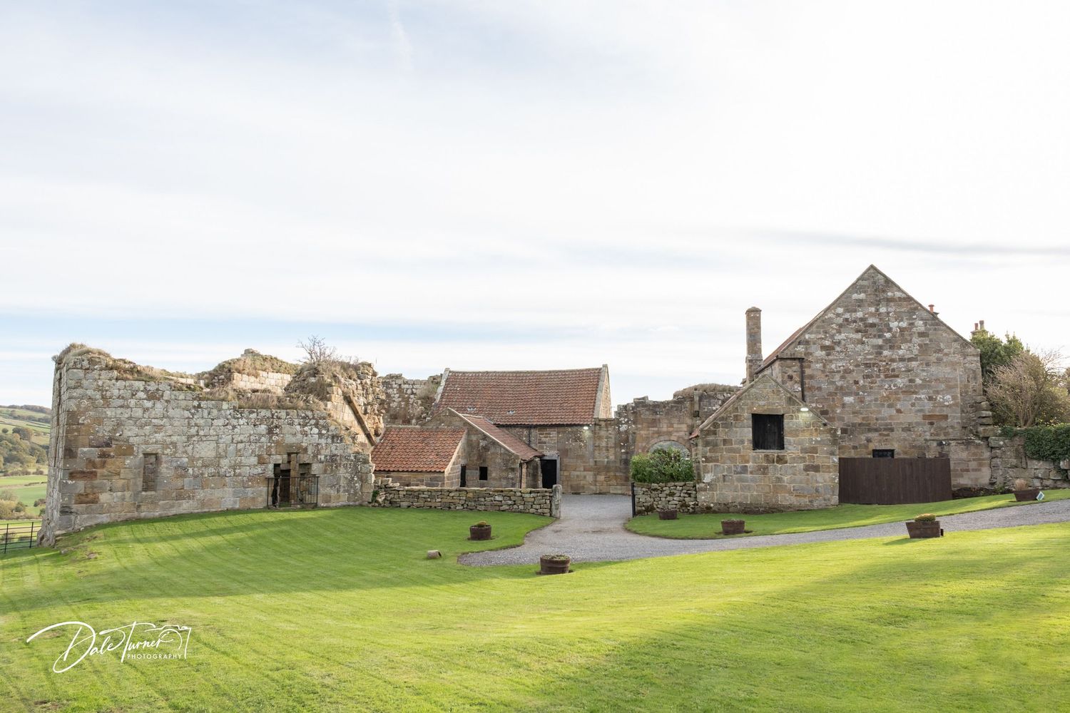 Panoramic view of abandoned stone buildings and ruins scattered across a grassy coastal landscape in Scotland.