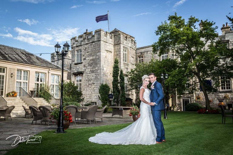 Wedding couple poses on manicured lawn with historic castle architecture backdrop.