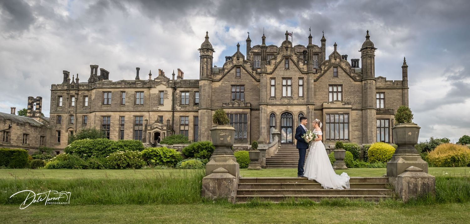 Exterior view of a grand historic stone castle building with Gothic architecture under dramatic cloudy skies.
