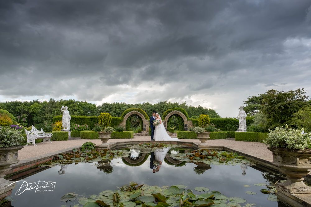 Reflective pond surrounded by manicured gardens and architecture creates perfect mirror image.