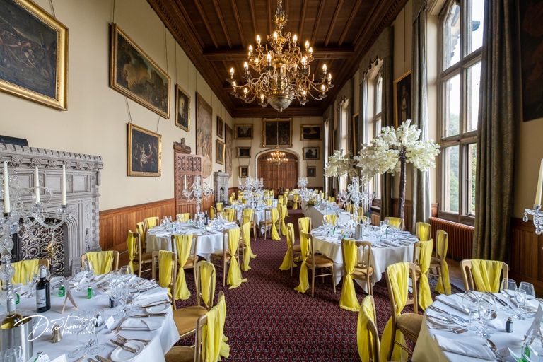 Panoramic view of formal dining room with chandeliers and yellow accented place settings.