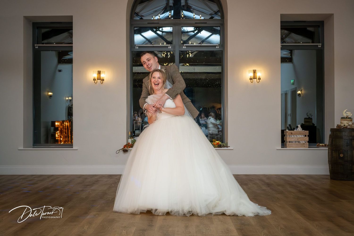A bride in a flowing white ballgown poses gracefully in an elegant venue with large windows and wall sconces.