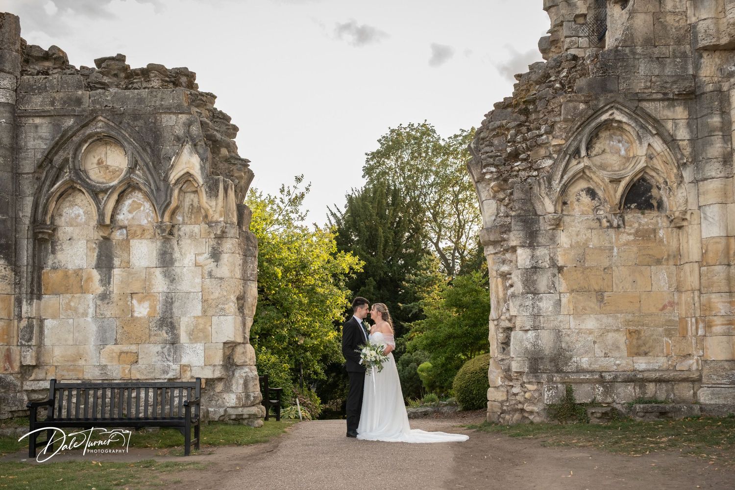 A wedding couple framed by gothic stone ruins and archways in a romantic setting.