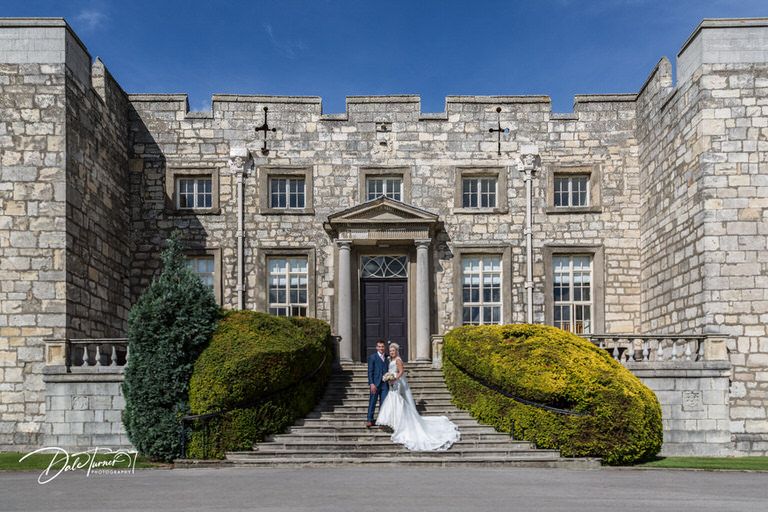 Panoramic view of grand stone castle with symmetrical architecture and manicured grounds.
