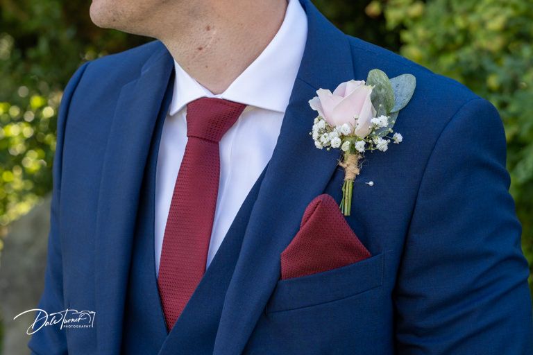 Close-up detail of a navy blue suit with red tie and pink floral boutonniere.