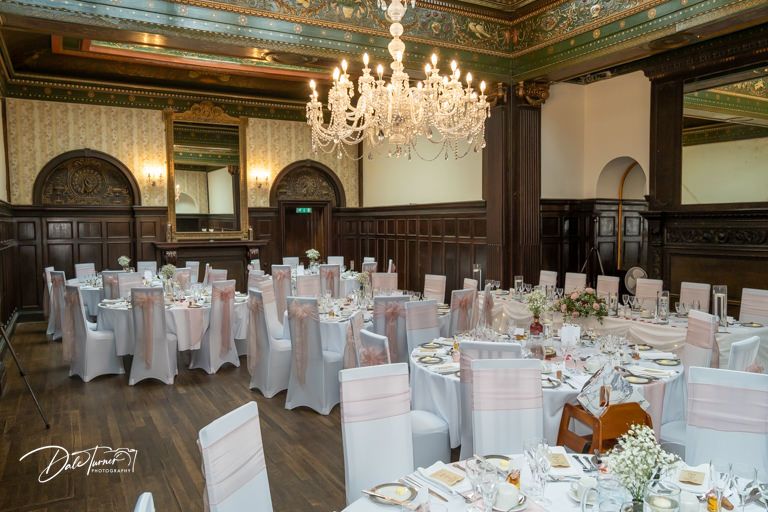 Elegant banquet hall with crystal chandeliers and white-covered tables set for a formal wedding reception.