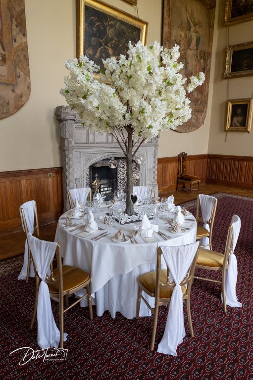 Intimate table setting with white floral centerpiece near an ornate fireplace in a historic dining room.