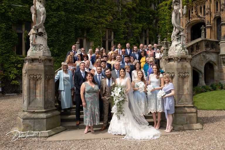 Wedding party poses for group photos along historic stone building facade.