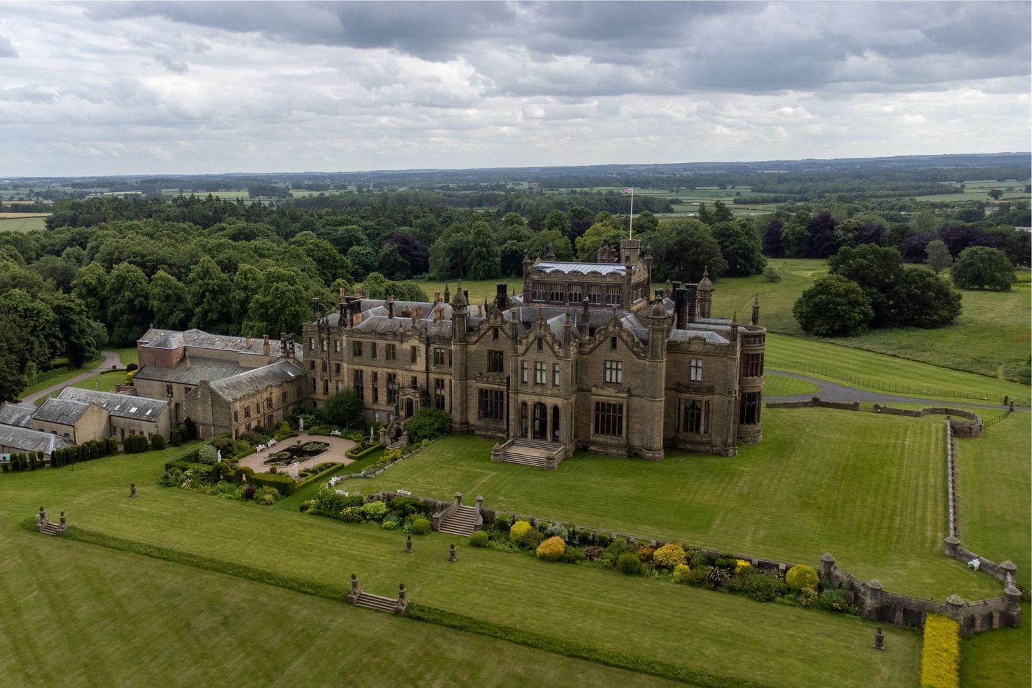 Panoramic aerial view of a grand historic estate with manicured lawns and Gothic architecture.