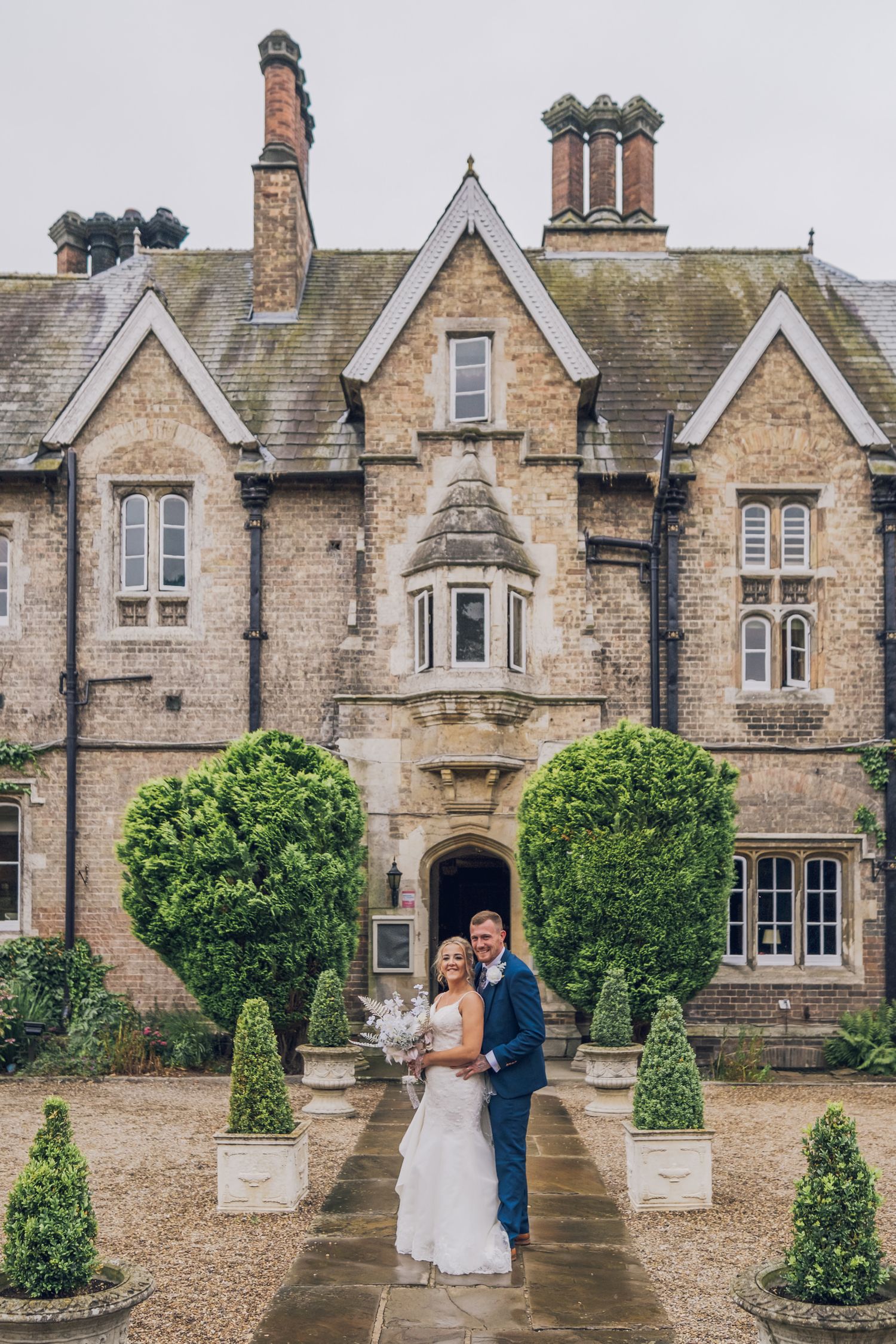 Elegant wedding photographs taken in front of a stunning Victorian stone mansion with manicured topiary.