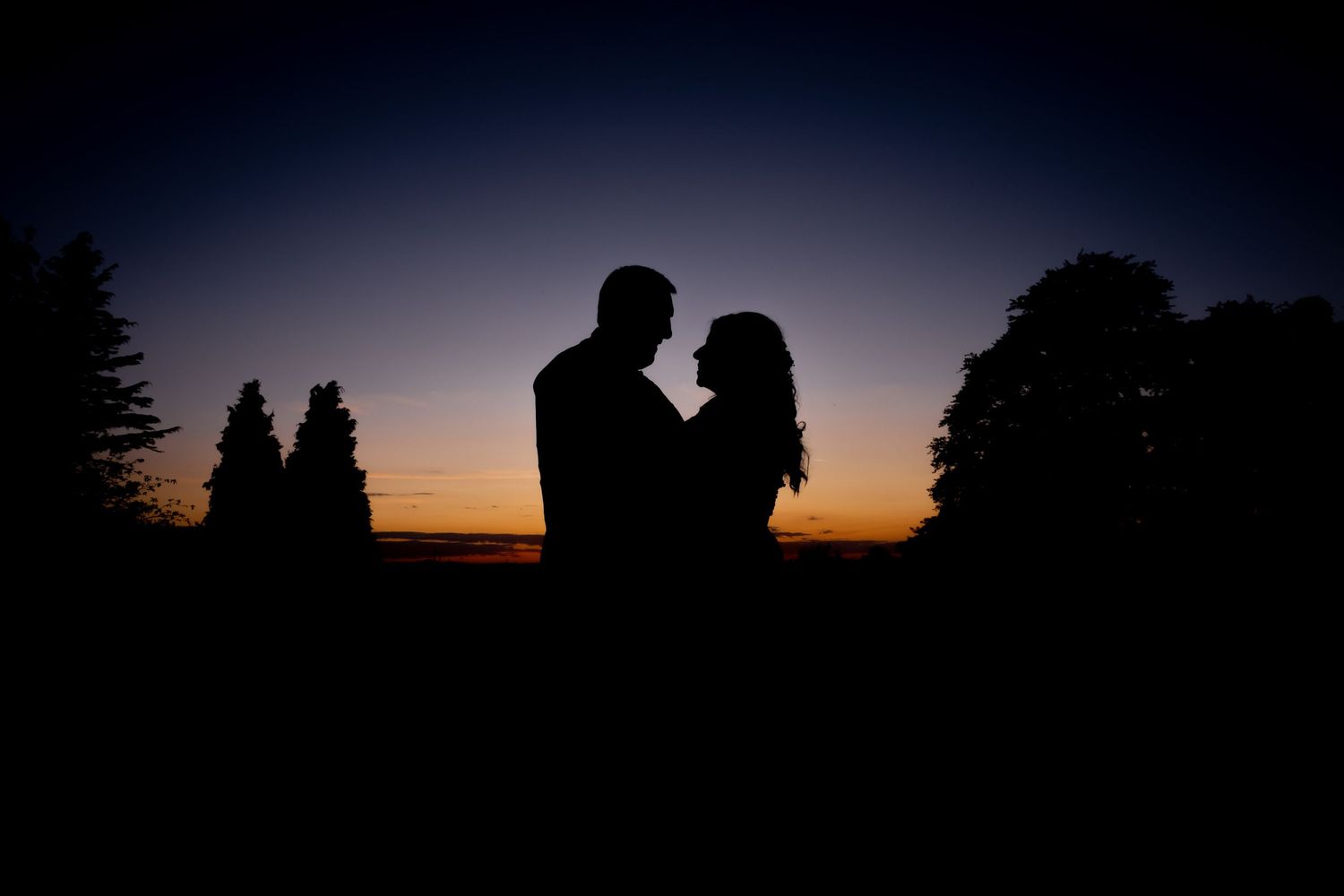 Silhouetted figures against dramatic sunset sky during outdoor wedding photography.