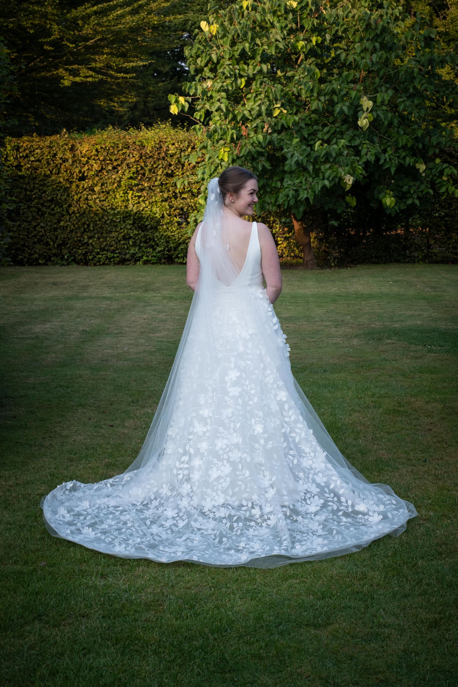 A stunning white lace wedding dress with a flowing train displayed on a green lawn in a garden setting.