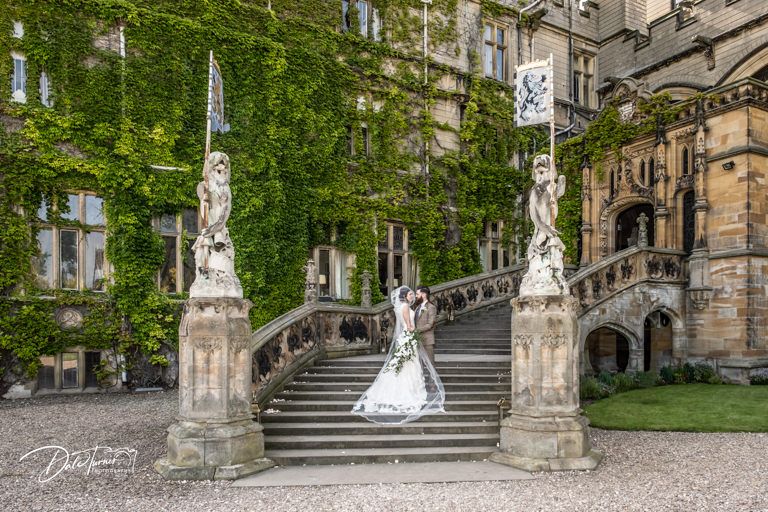 Wedding portrait on grand stone staircase with ornate pillars and ivy-covered walls.
