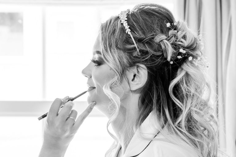 Getting ready scene in black and white showing final wedding preparations and makeup application.