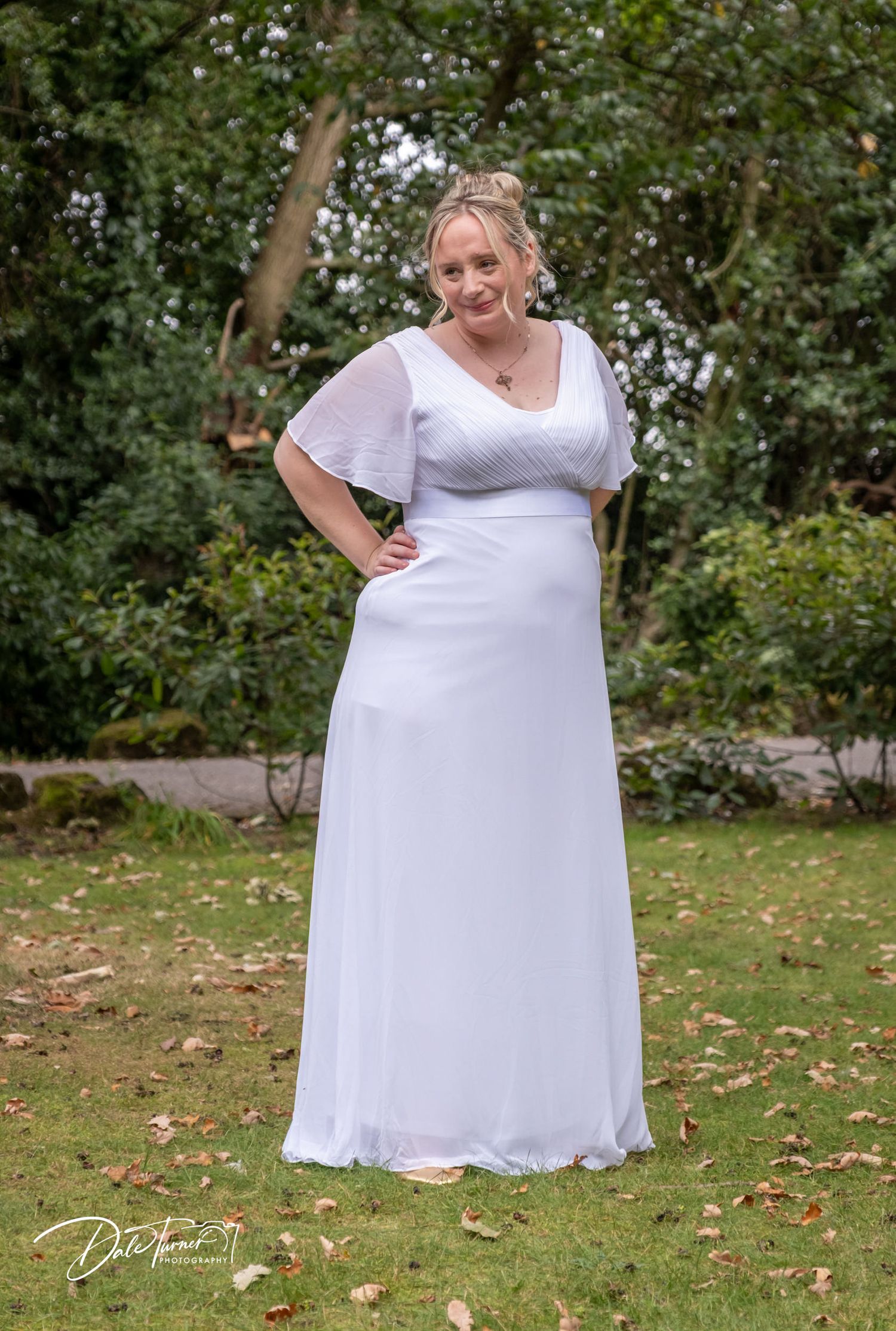 Person in flowing white wedding dress poses elegantly in a garden setting.