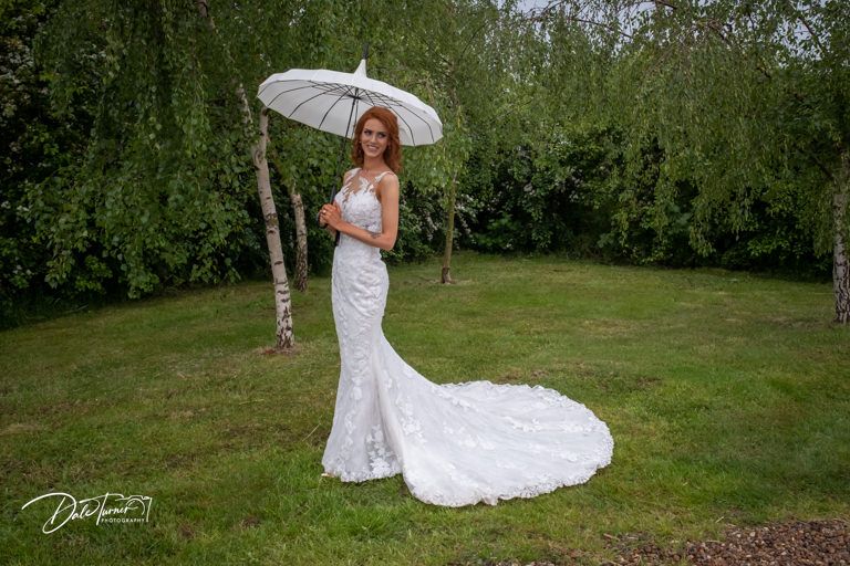 Elegant bride with parasol poses in a natural garden setting.