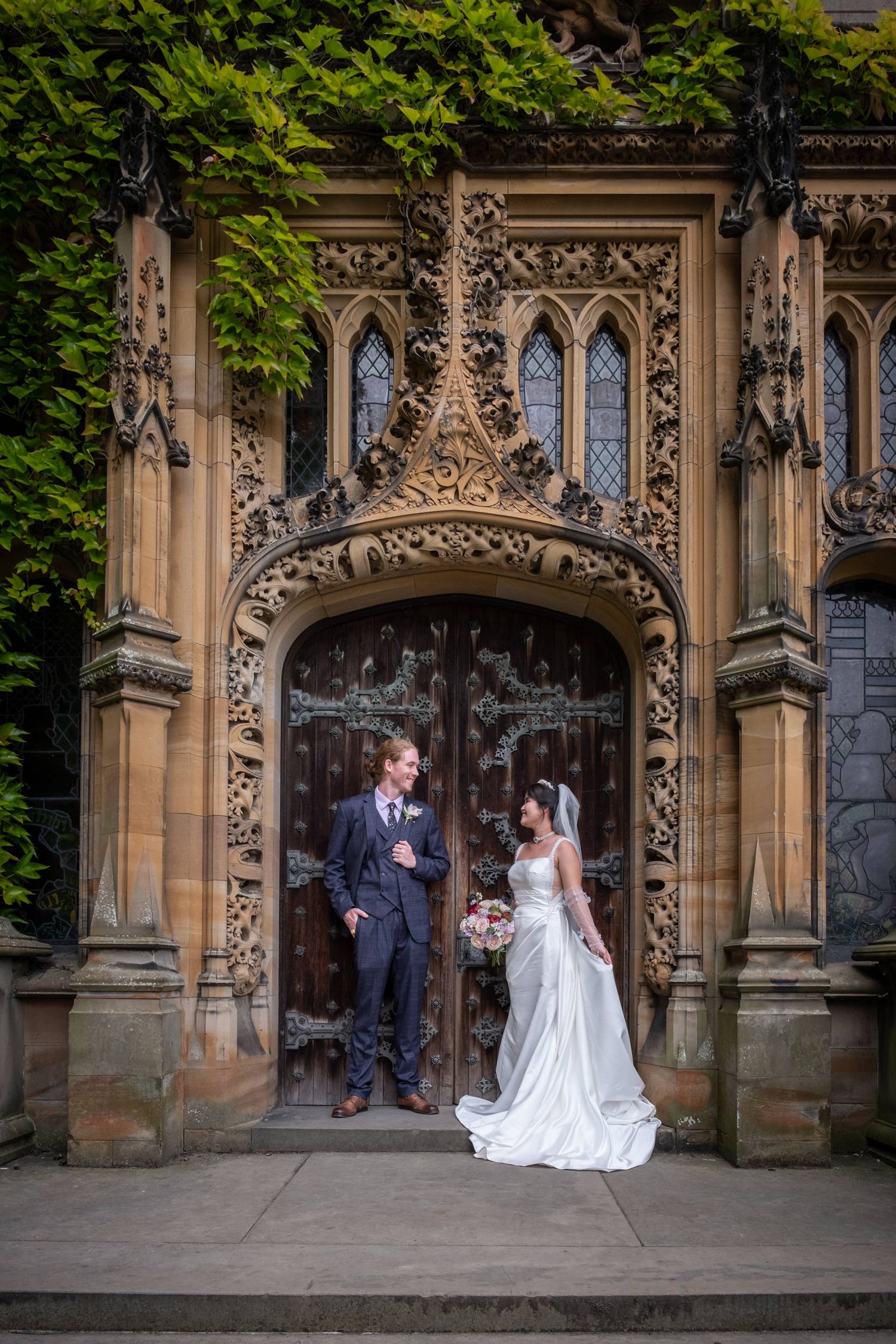 Elegant wedding scene at ornate gothic entrance with stone archway and decorative carvings.
