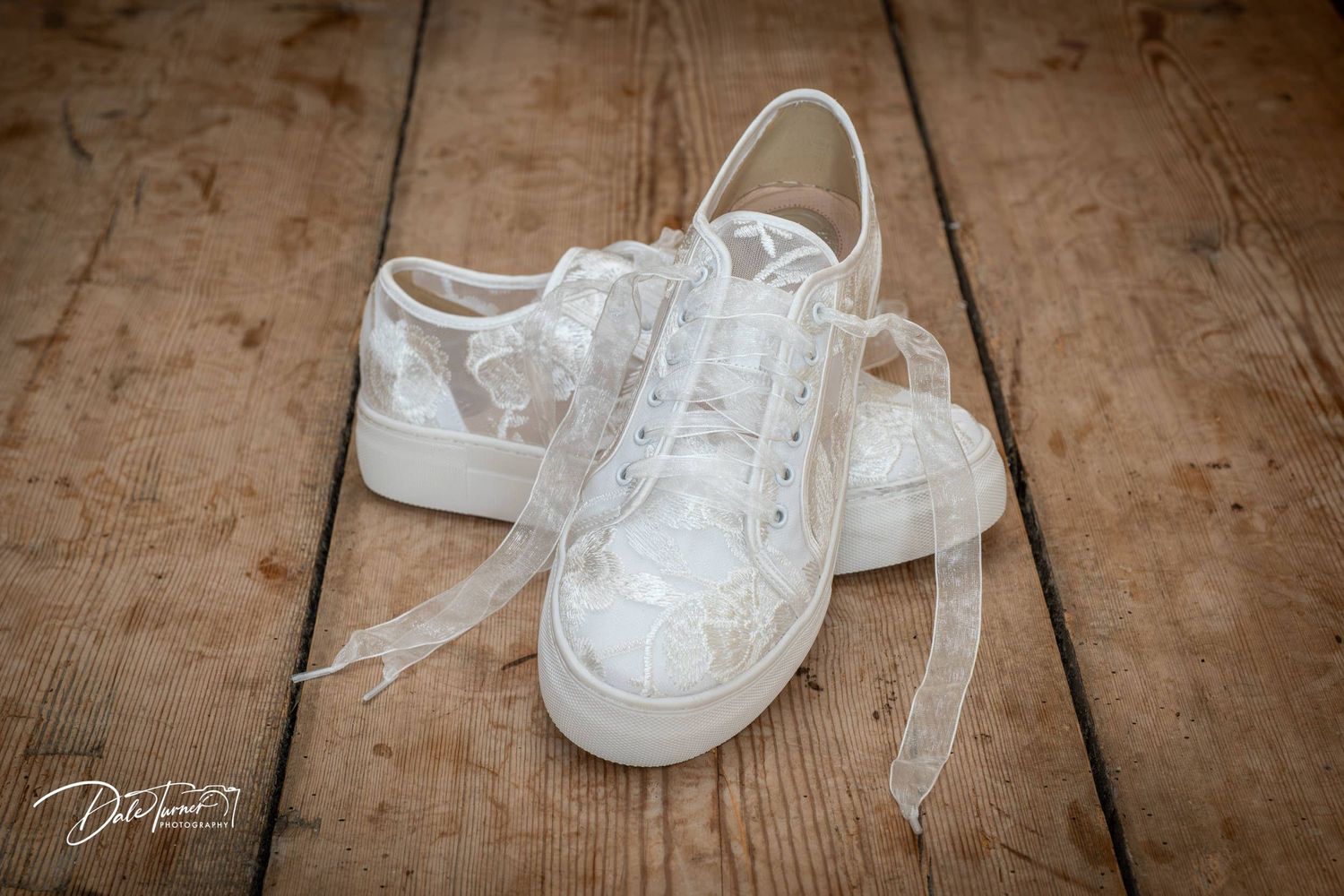 White wedding sneakers with delicate lace ribbons arranged in sequence on rustic wooden floor.