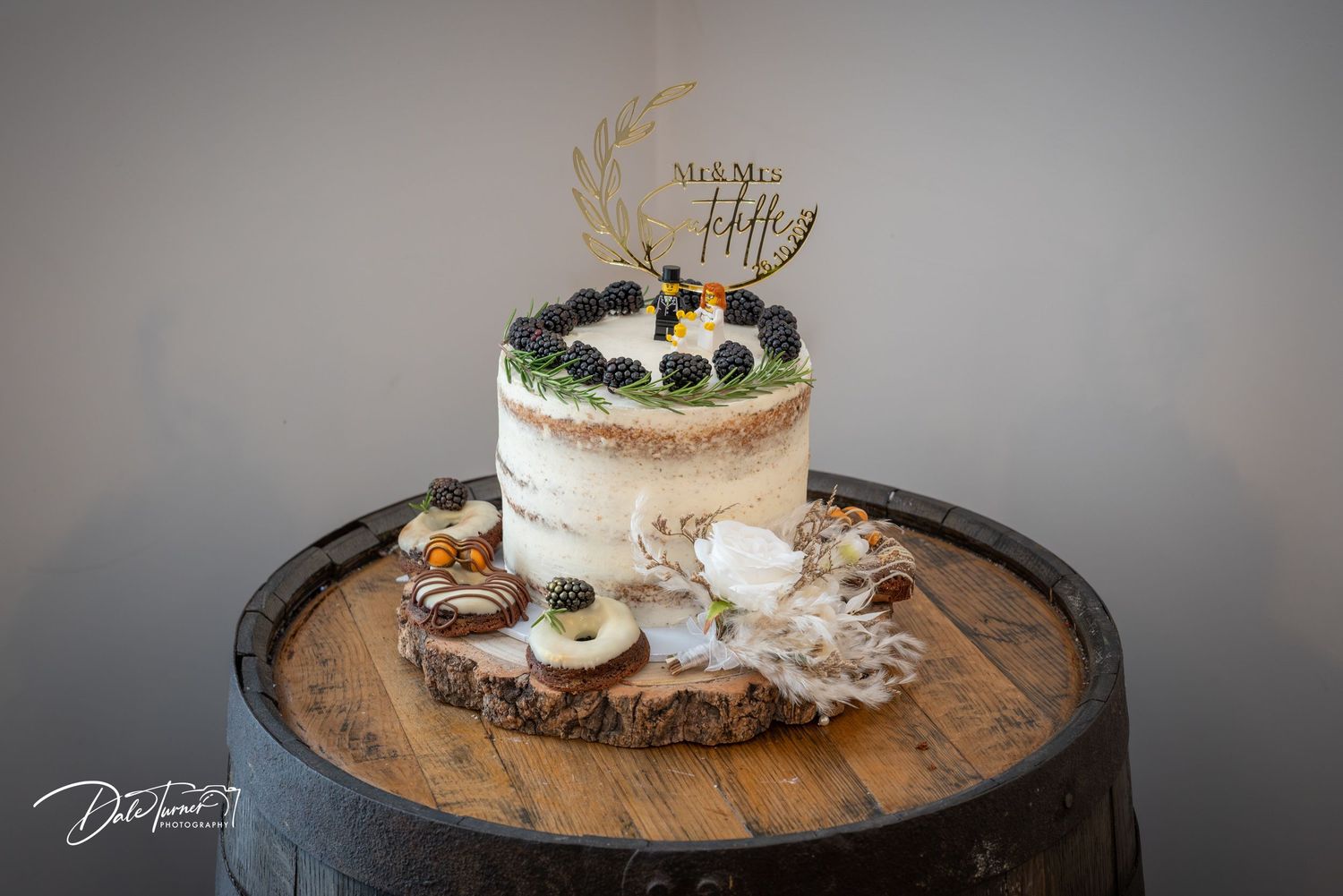 Rustic wooden barrel displays a white frosted cake adorned with delicate floral decorations and fresh flowers on top.