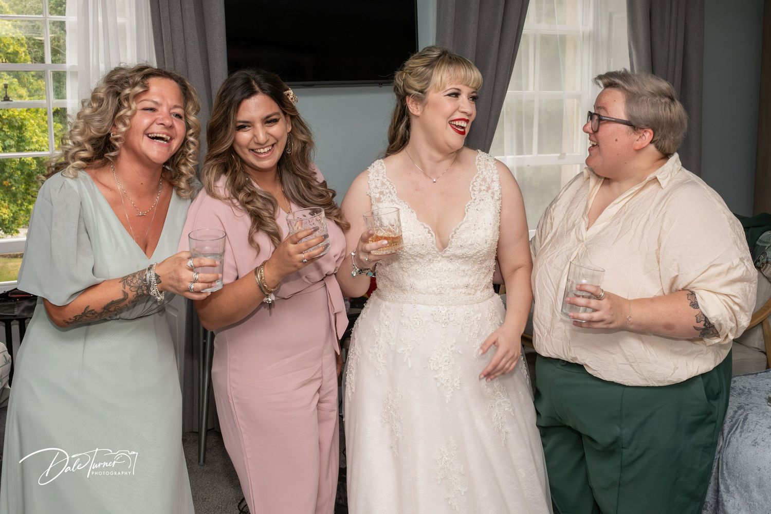 Wedding party members in pink and green dresses share joyful moments together during celebration.