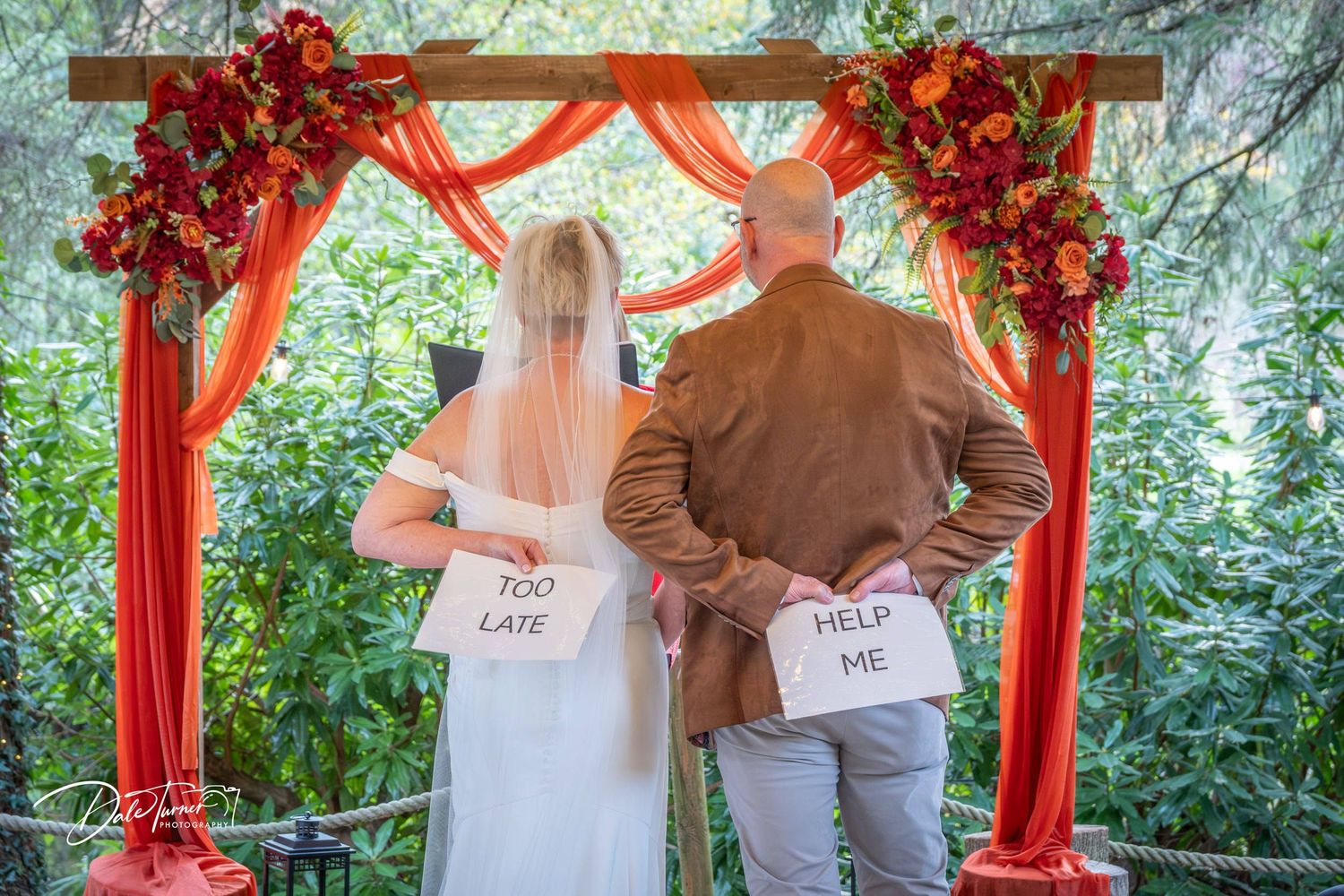 Wedding ceremony scene with red floral arch and natural greenery backdrop.