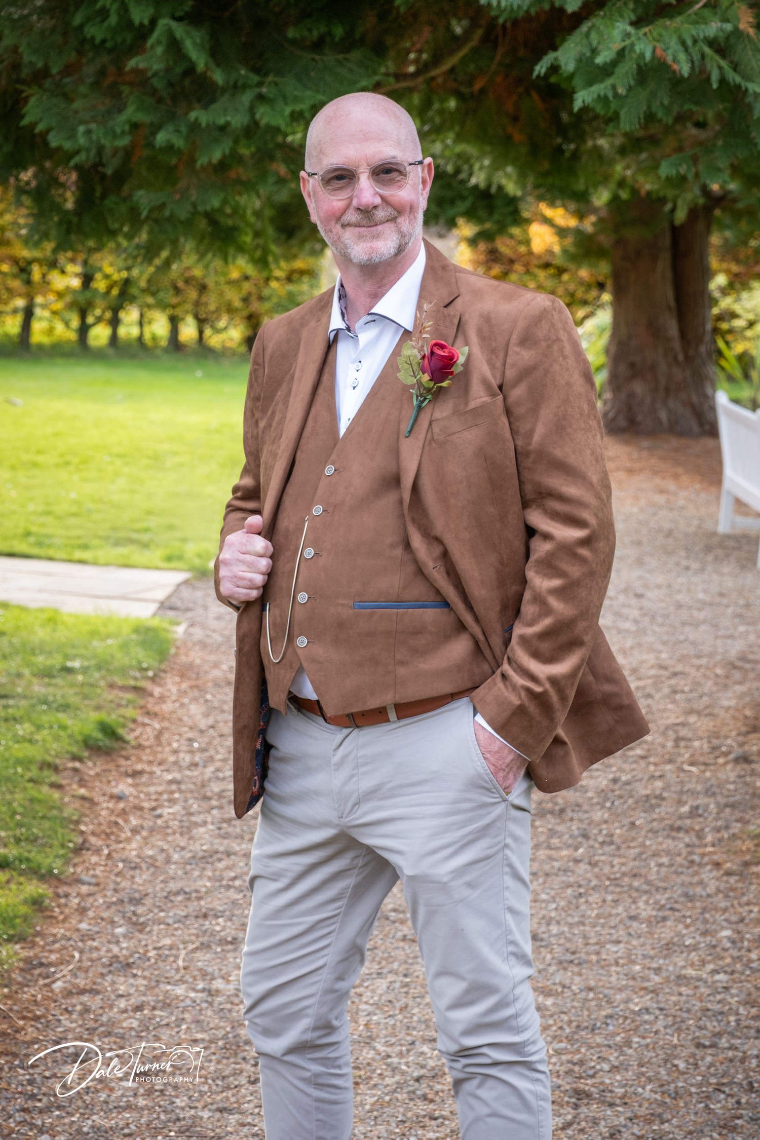 Person in brown tweed jacket and light pants posing on garden path.