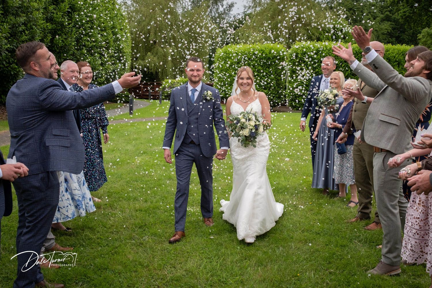 Wedding guests celebrating and throwing confetti in a lush garden setting.