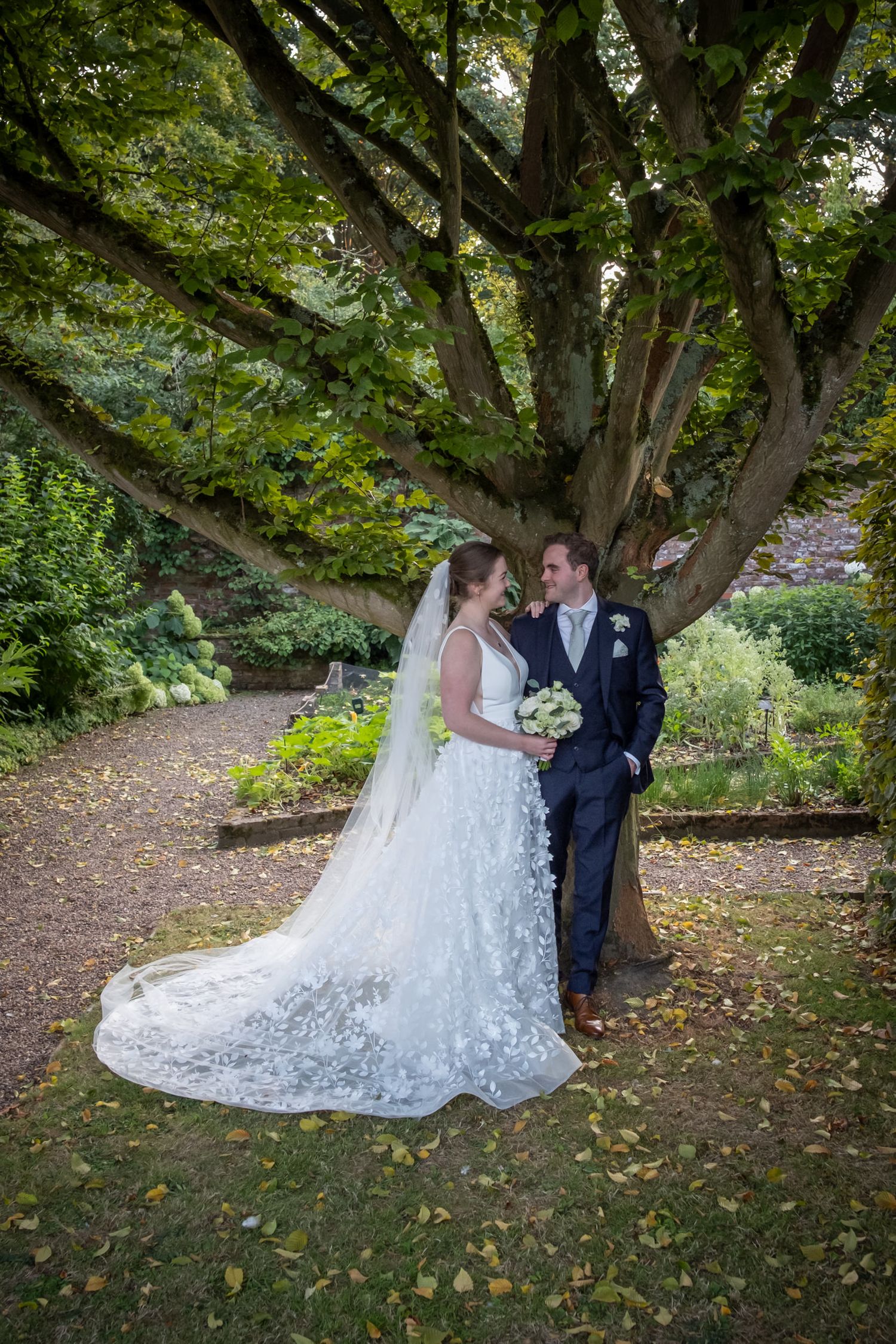 A romantic wedding moment captured under tree branches in an autumn garden setting.