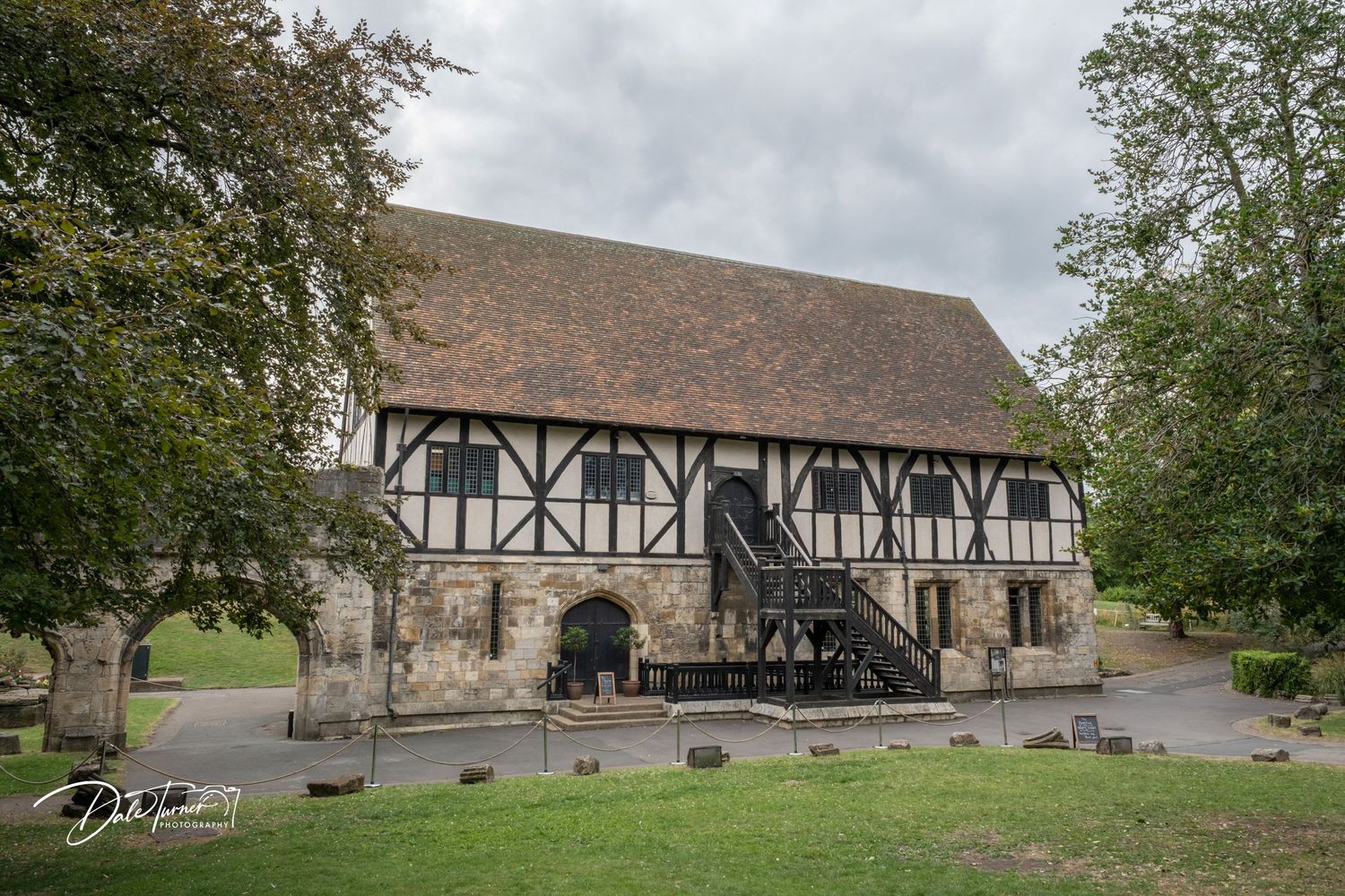 Exterior view of a historic Tudor-style stone and timber building surrounded by trees.