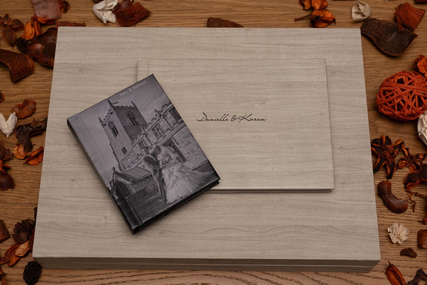 Wedding photo album and prints displayed on wooden surface with decorative elements.