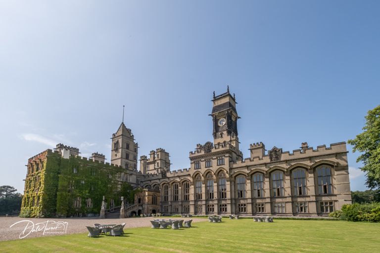 Majestic Victorian Gothic castle with towers and ivy-covered walls under blue sky.