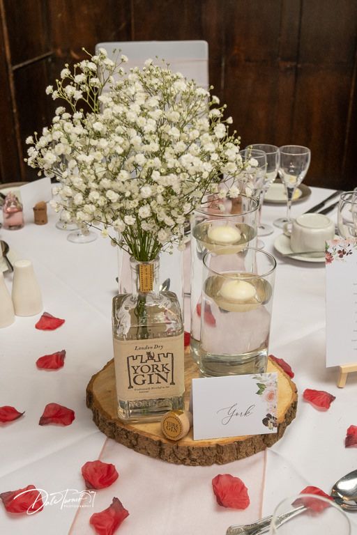Rustic wedding centerpiece featuring baby's breath in glass vases on wooden slice with name cards.