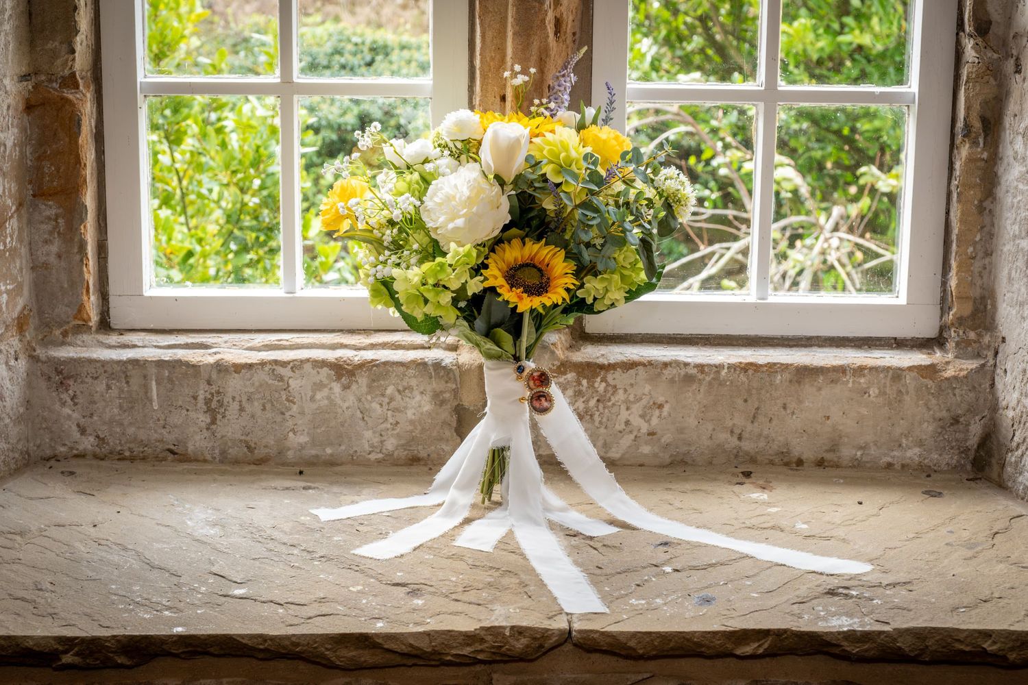 Rustic stone windowsill decorated with sunflowers in glass vases and white ribbons creating an elegant farmhouse display.