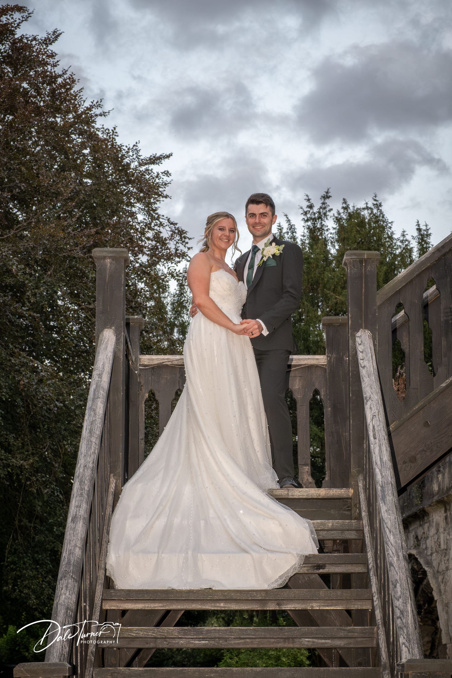 Wedding couple poses on wooden stairs against a moody sky backdrop.