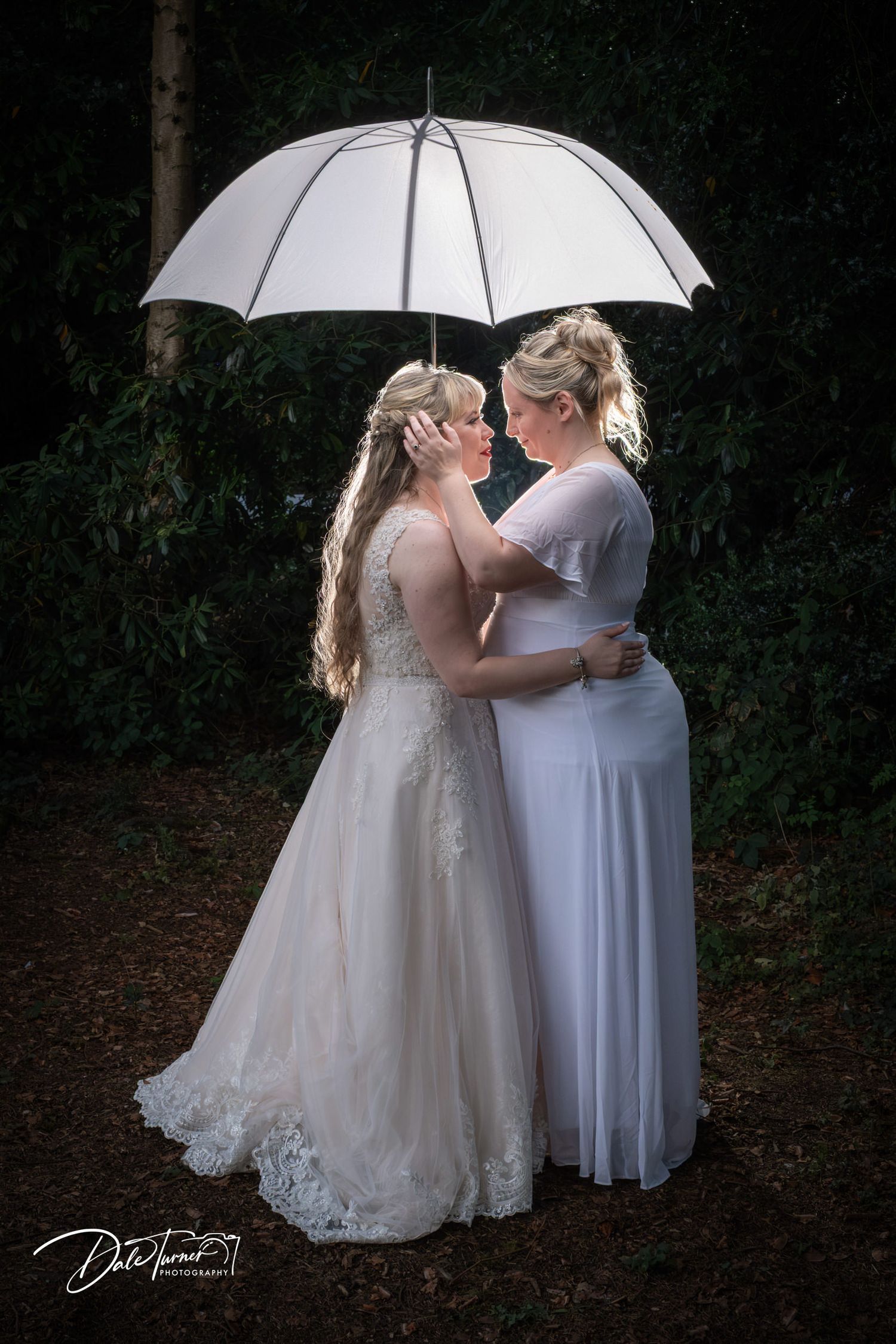 Wedding couple sharing intimate moments under a white umbrella in a garden setting.