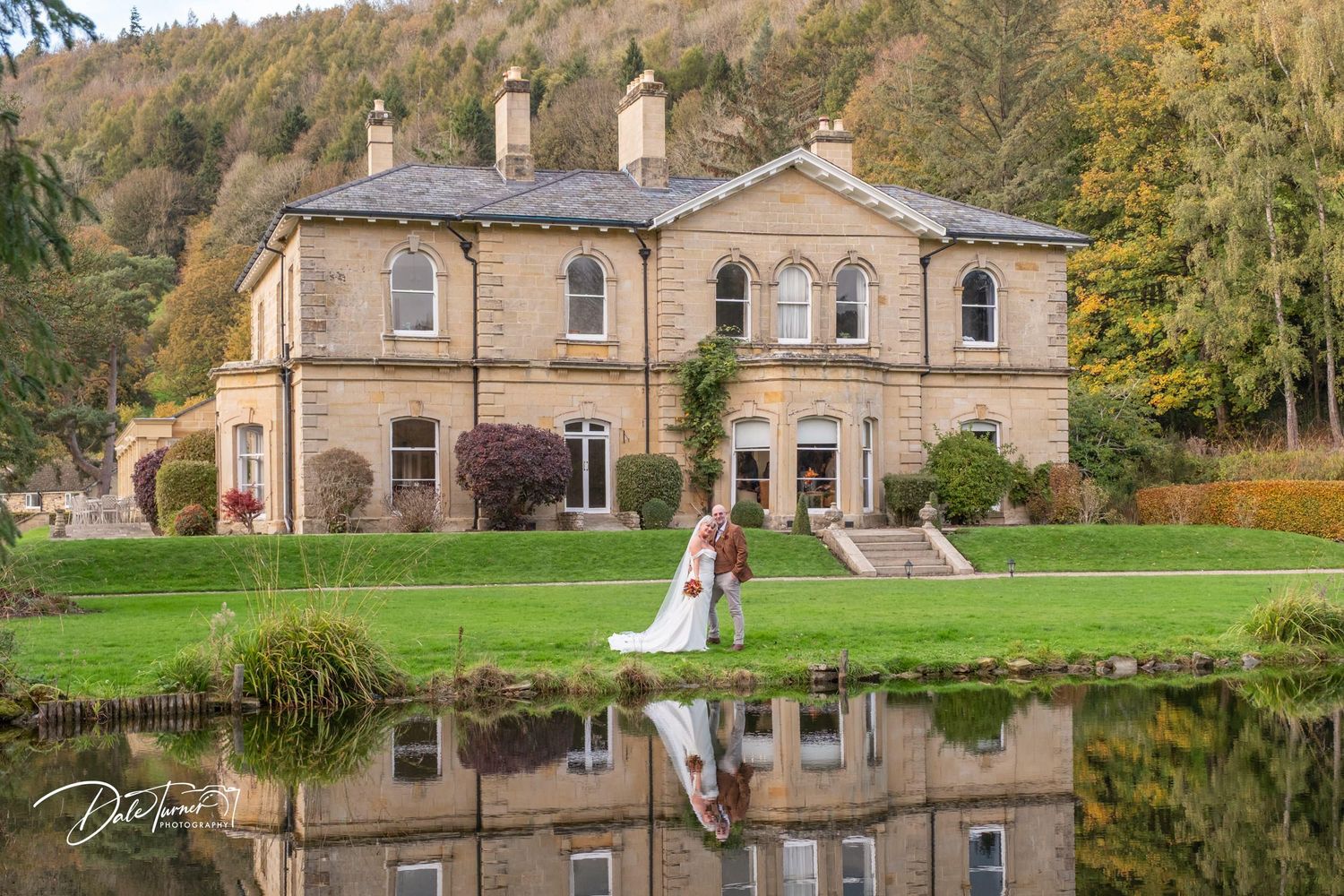 Stone mansion with symmetrical architecture reflected in tranquil pond during autumn.