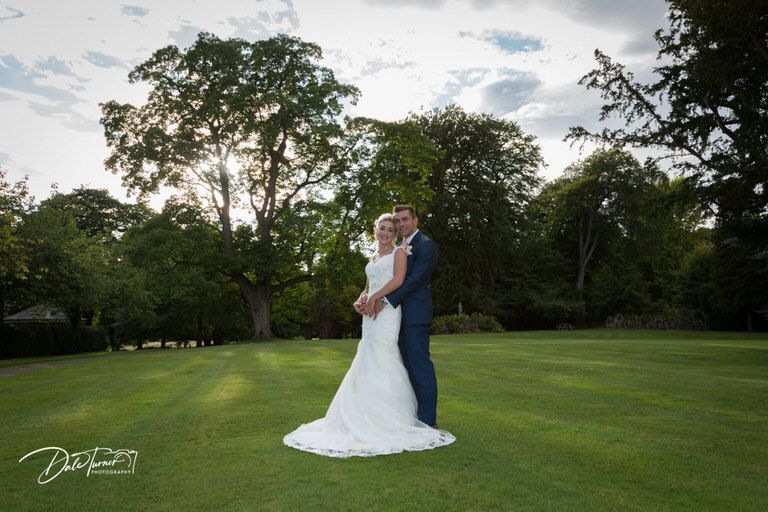 Panoramic view of wedding couple celebrating on sprawling garden grounds.