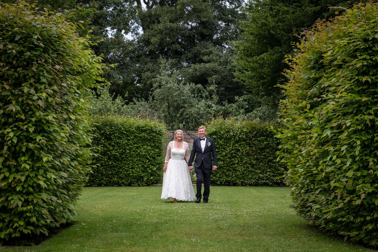 Manicured garden pathway with tall green hedges creating a romantic wedding photo setting.