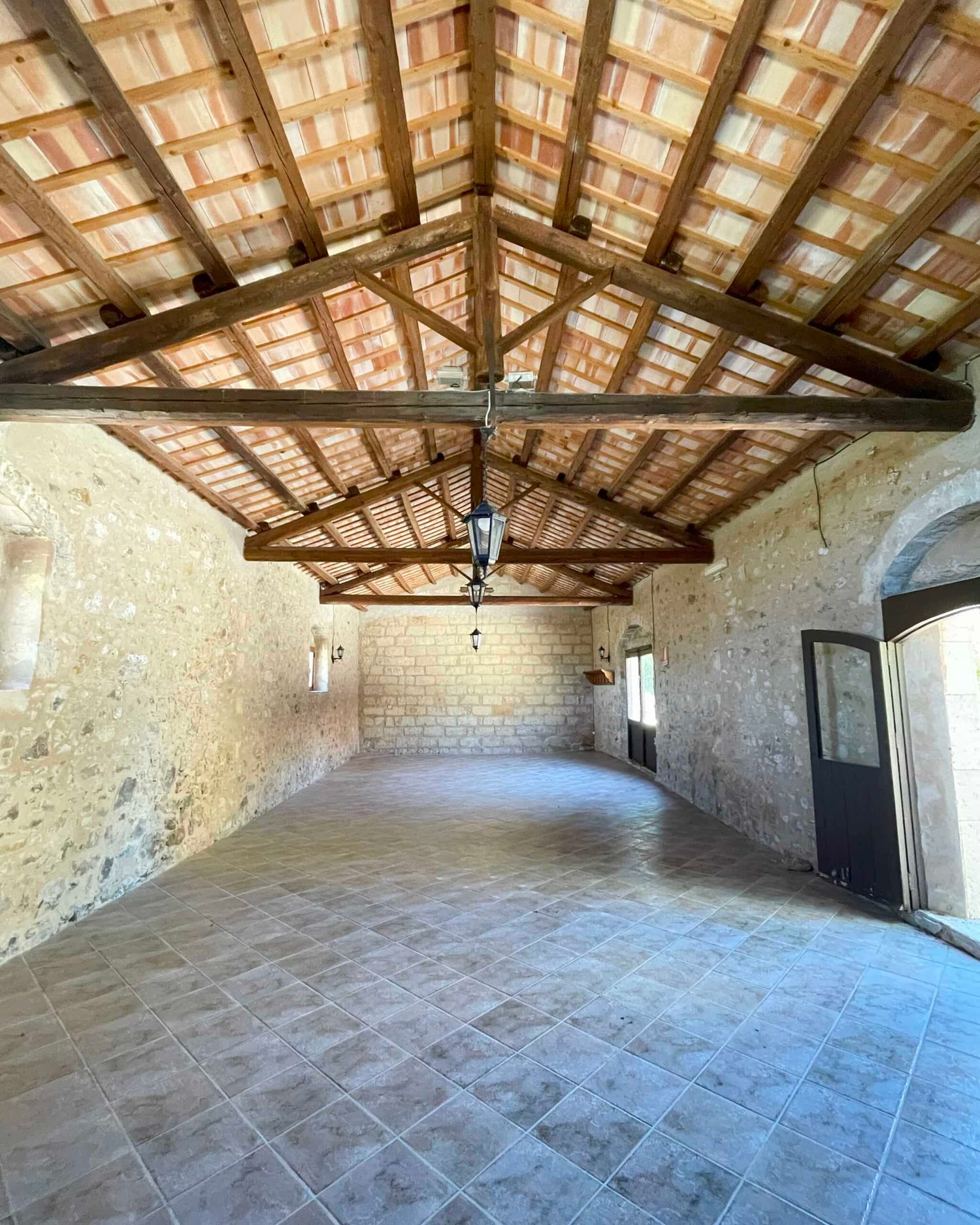 Spacious empty stone barn interior with exposed wooden beam vaulted ceiling and tiled floor, ready for renovation.