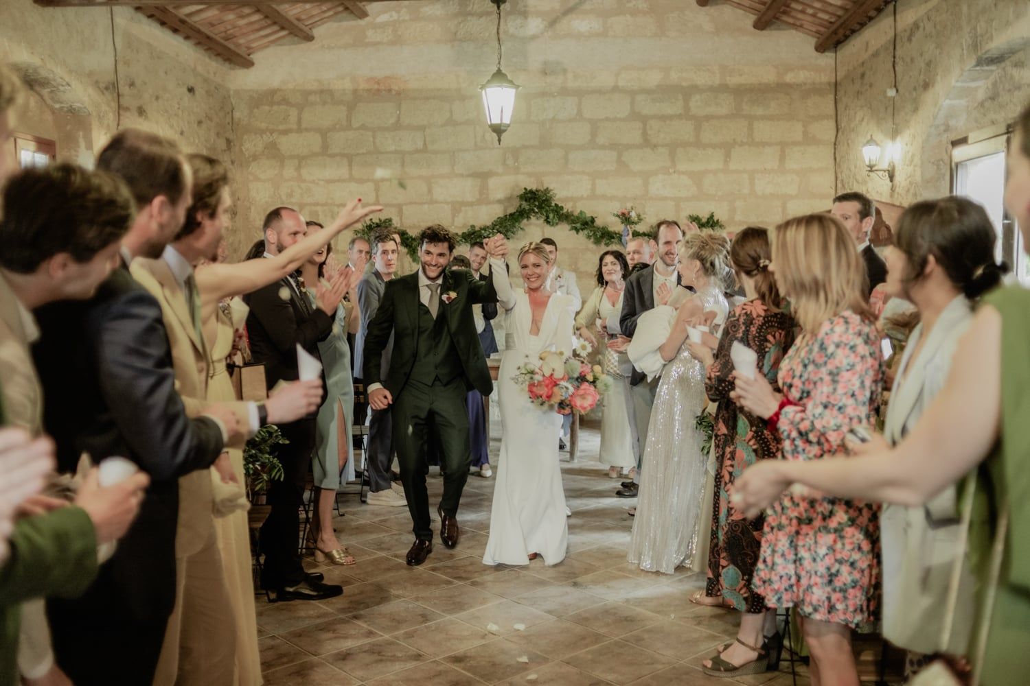 Joyful newlyweds walk through confetti-filled stone barn as guests celebrate their wedding reception exit together.
